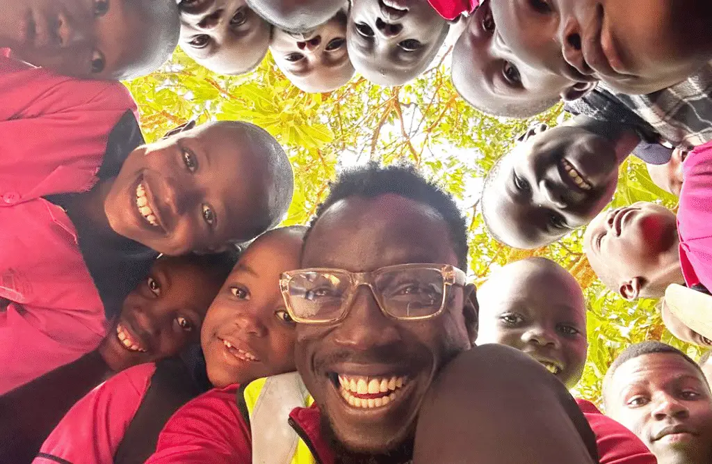 A group of people are gathered around a camera beneath them, smiling